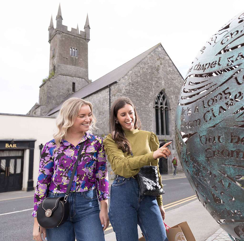 Two women at bronze monument with old church in background
