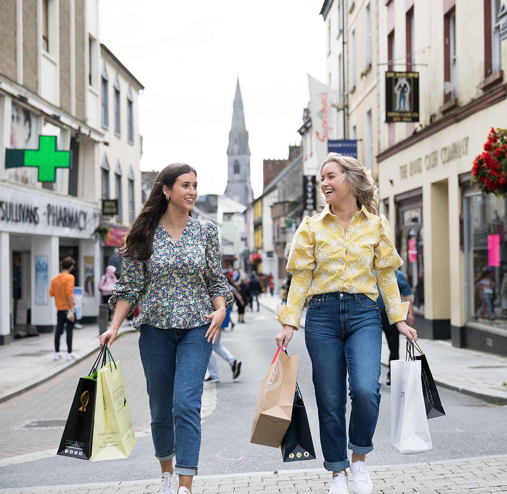 Two women with shopping bags walking in O'Connell Street with cathedral in background