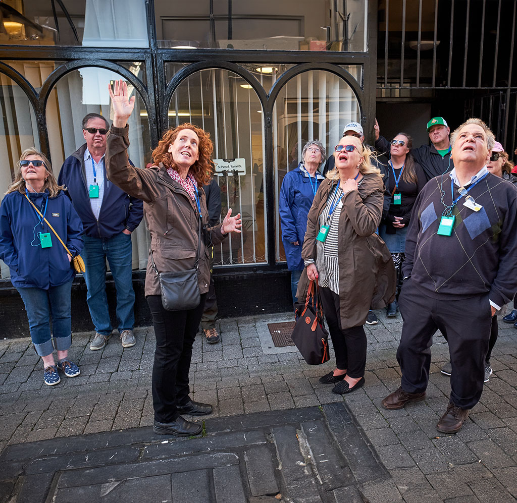 Jane with tour group in front of shop, pointing up